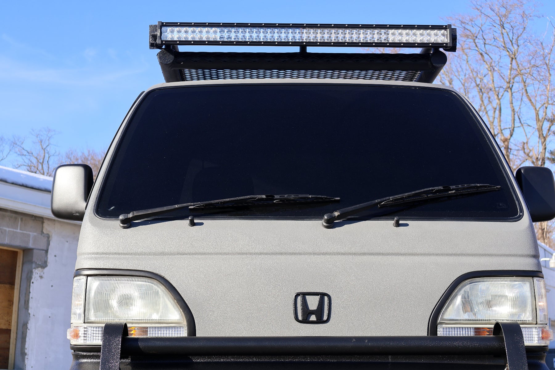 Front view of a Honda mini truck with roof lights against a clear blue sky.