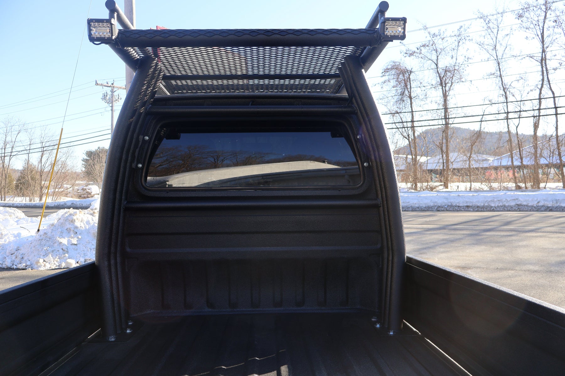 Back of a mini truck bed with a roof rack in a snowy landscape.