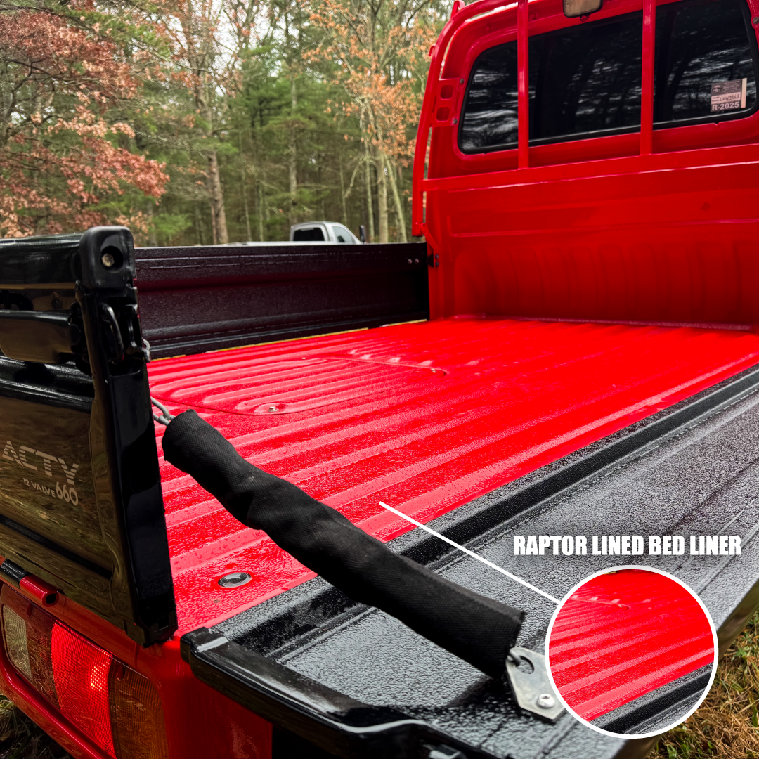 Red truck bed with black Raptor lined bed liner in a forest setting