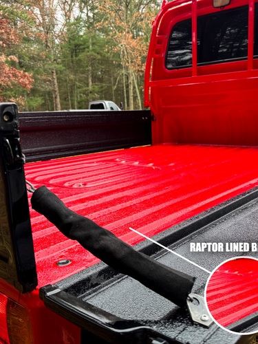 Red truck bed with black Raptor lined bed liner in a forest setting