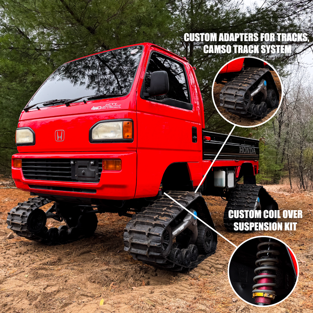 Red Honda truck with custom track system and suspension kit on a dirt road.