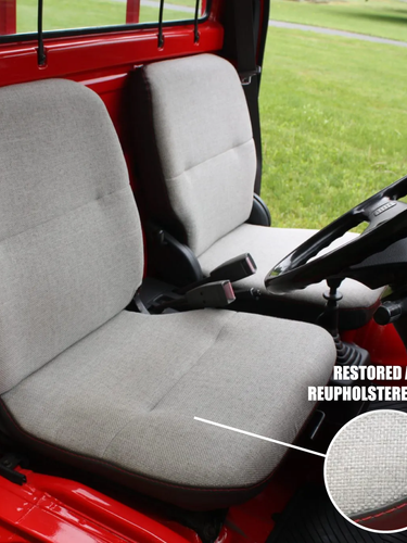 Gray restored and reupholstered seats inside a red vehicle with grass outside.