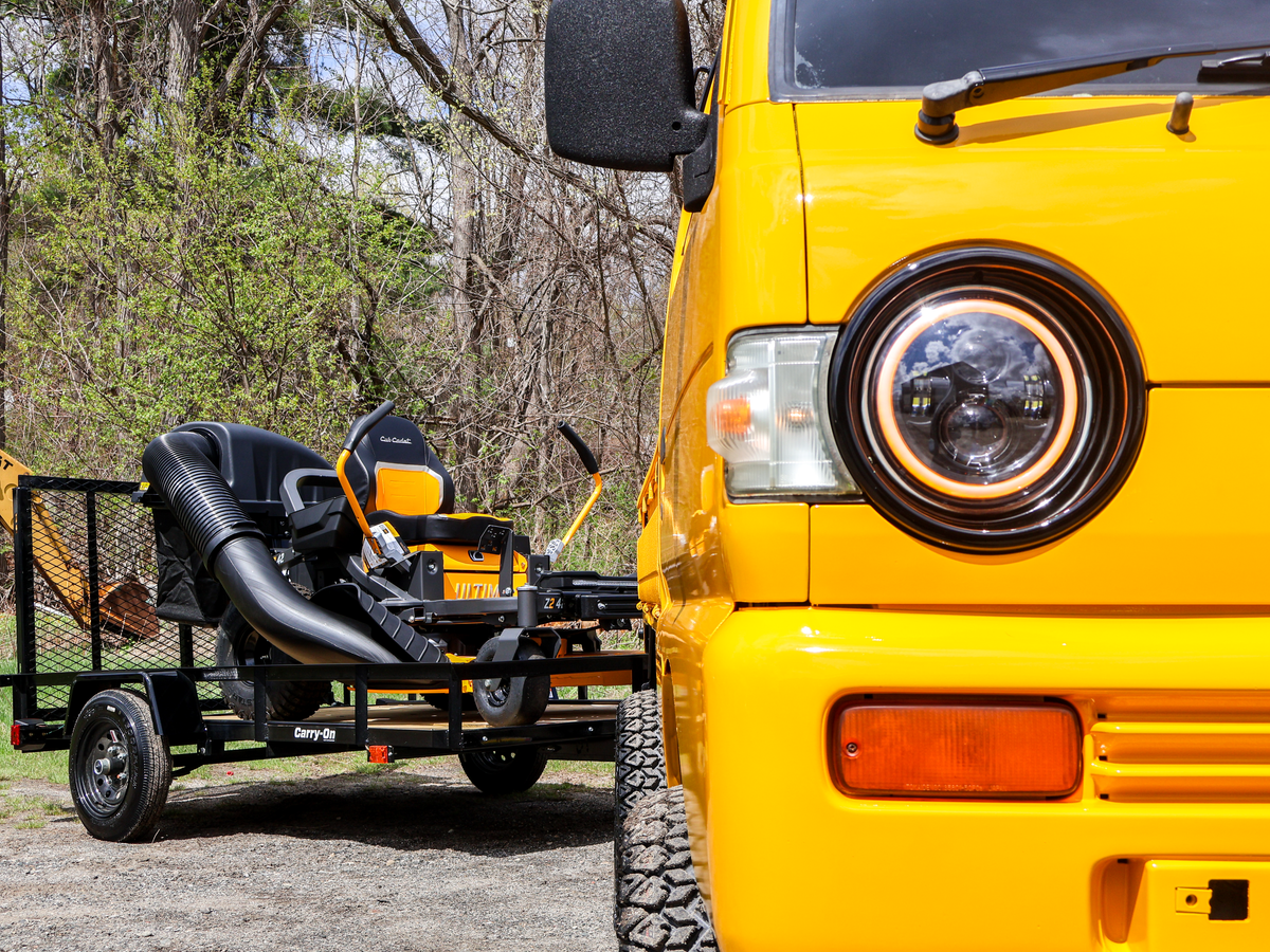 Yellow truck towing a trailer with lawn equipment in a wooded area