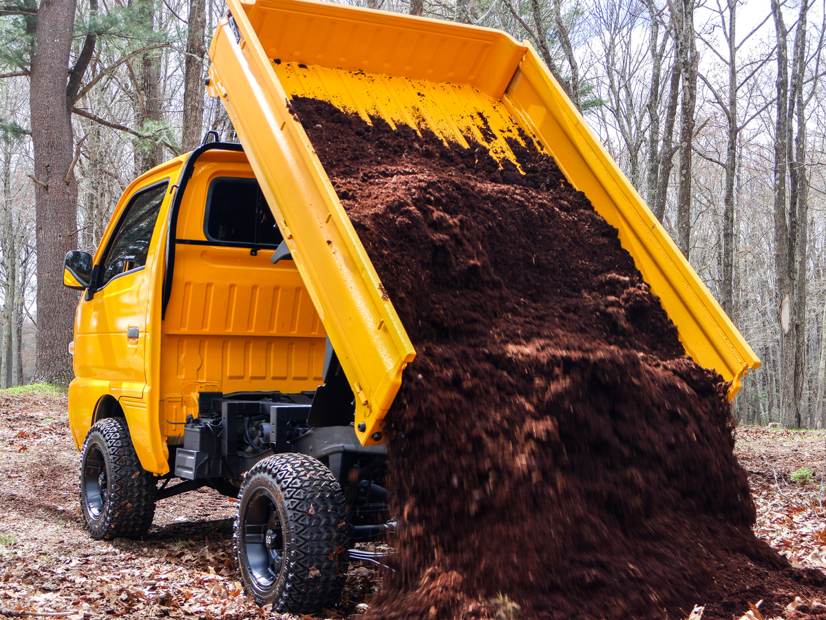 Yellow dump truck tipping a load of dirt in a forest setting