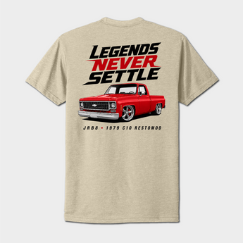A light beige heather t-shirt showing the back graphic print. The design features the text 'LEGENDS NEVER SETTLE' in black and red, above a graphic of a red 1979 Chevrolet C10 Restomod truck, with 'JRB 1979 C10 RESTOMOD' printed below.
